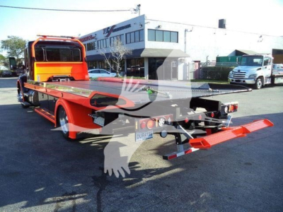 Kenworth T280 rollback tow truck rear view showing bed and red ramps with black chassis and orange cab in a dealership lot.