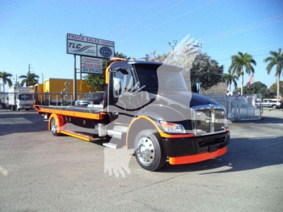 Kenworth T280 tow truck/rollback in a dealership lot, front cab and orange chassis visible with a side deck.