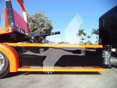 Kenworth truck side view showing side underride step with orange and black color, part of rollback equipment, cab and wheel in frame.