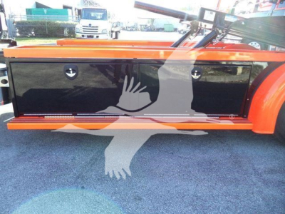 Kenworth truck side toolbox with glossy black panels and orange body. Two circular access doors on the panel. Reflection of a hand-shaped watermark overlay.