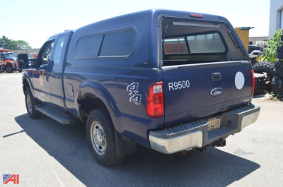 Ford F-250 Super Duty pickup truck rear-side view showing blue crew cab with camper shell, 4x4 badge, R3500 model text, and Ford emblem.
