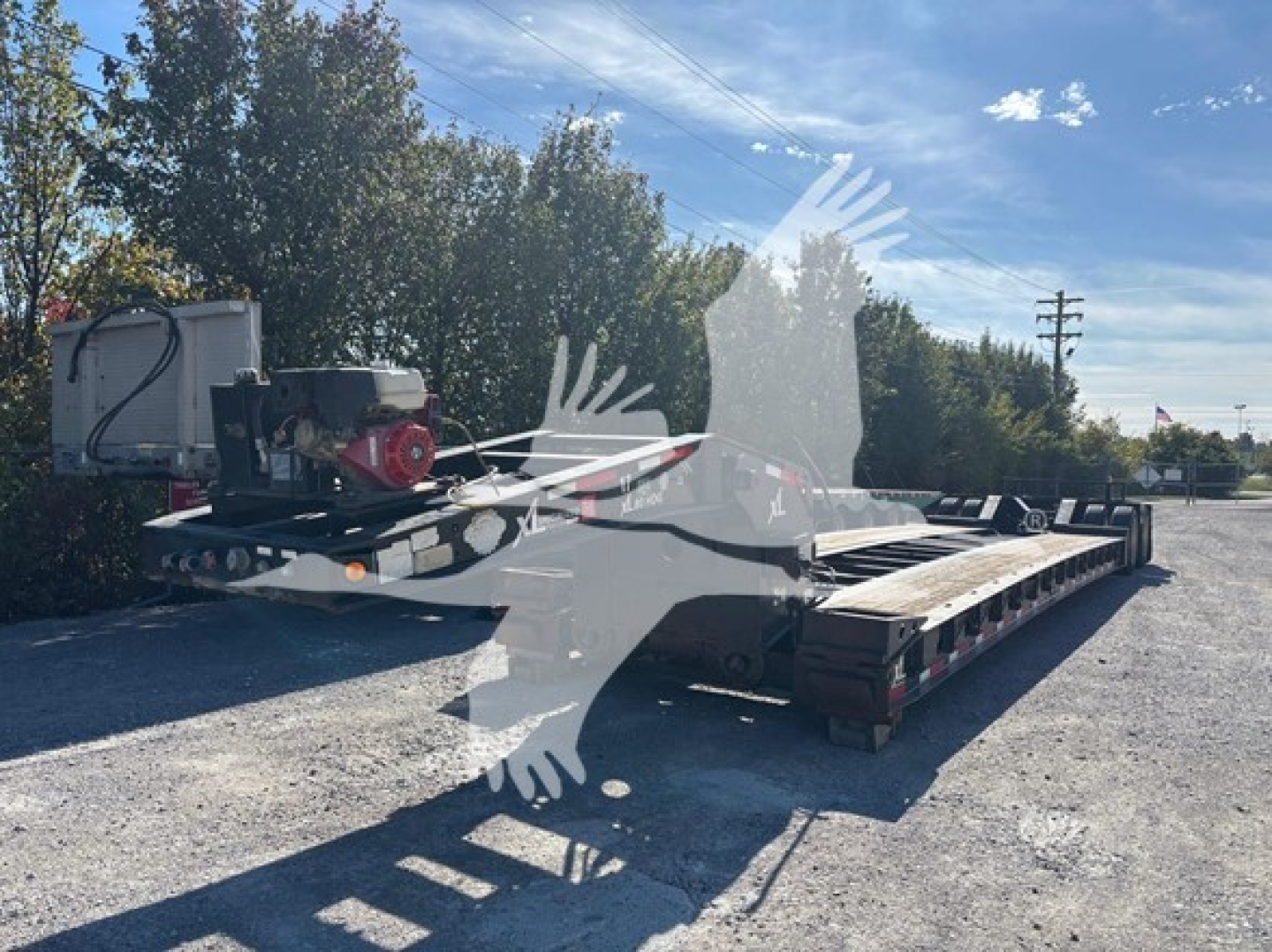 Flatbed trailer with a red generator on the front deck, lowboy trailer with multiple axles and black frame, outdoor lot.