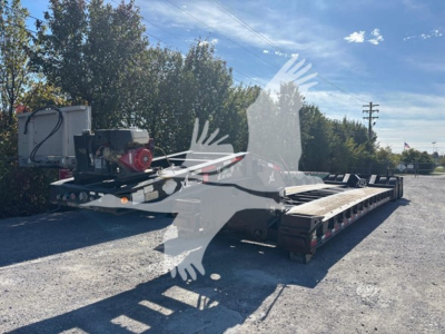 Flatbed trailer with a red generator on the front deck, lowboy trailer with multiple axles and black frame, outdoor lot.