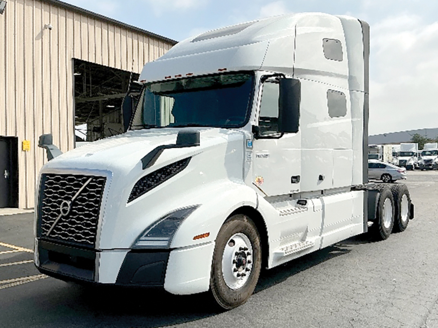 Volvo VNL 760 semi truck tractor in a dealership lot, white exterior, sleeper cab, front grille with Volvo emblem, dual rear axles, side mirrors, windows.