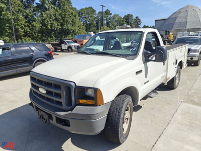 White 2006 Ford F-350 utility/service truck in a parking lot, long flatbed/utility bed, front grille with Ford badge, black bumper, large side mirrors, daytime.