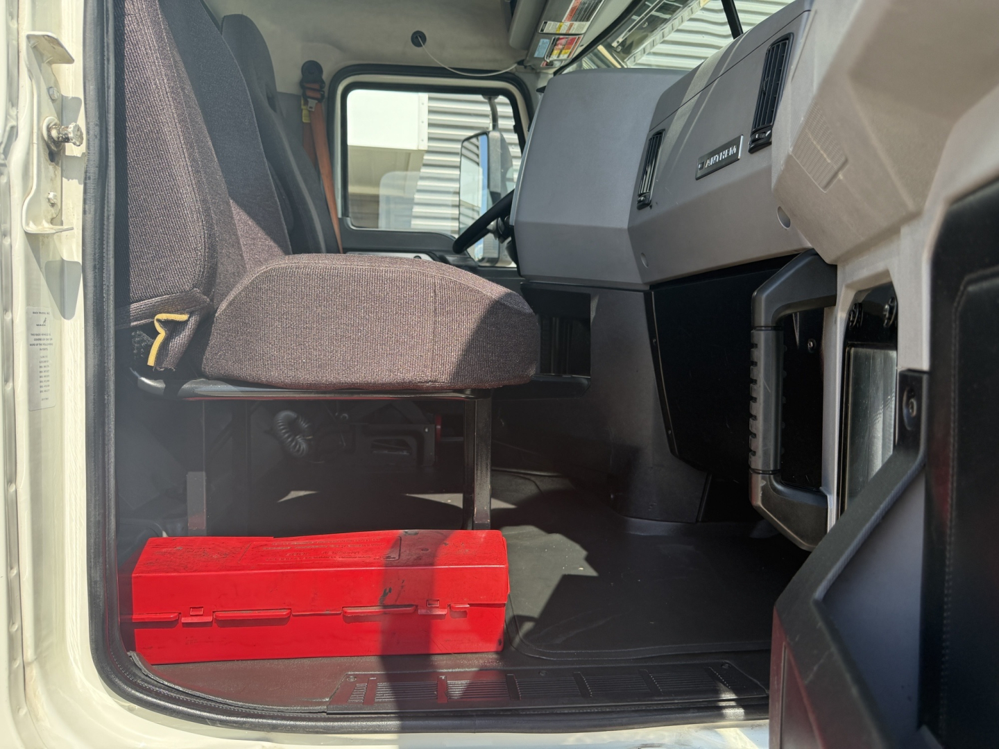 Cab interior of a 2020 Mack AN64T daycab showing driver seat, dashboard, and a red toolbox on the floor.