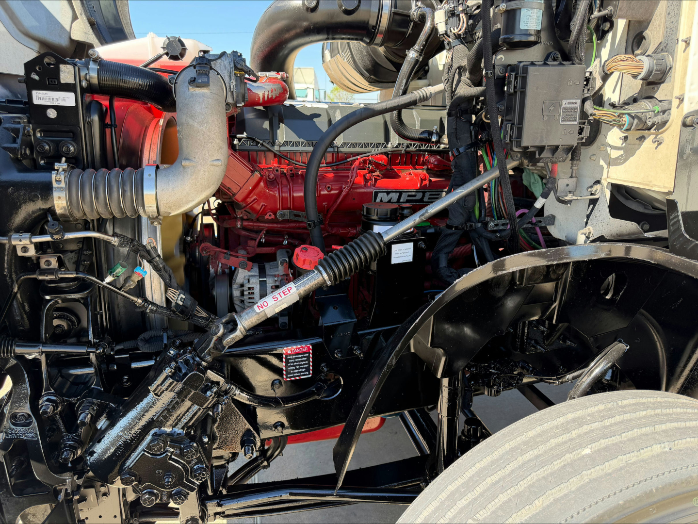 Engine bay of a 2020 Mack AN64T conventional daycab showing red engine block and surrounding hoses, hoses, and components.