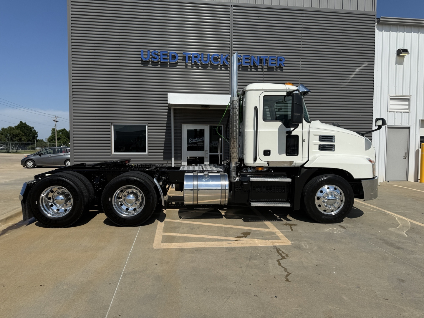 Truck side view showing 2020 Mack AN64T conventional daycab with white cab, dual rear axles, fuel tank, and wheel rims in front of used truck center.