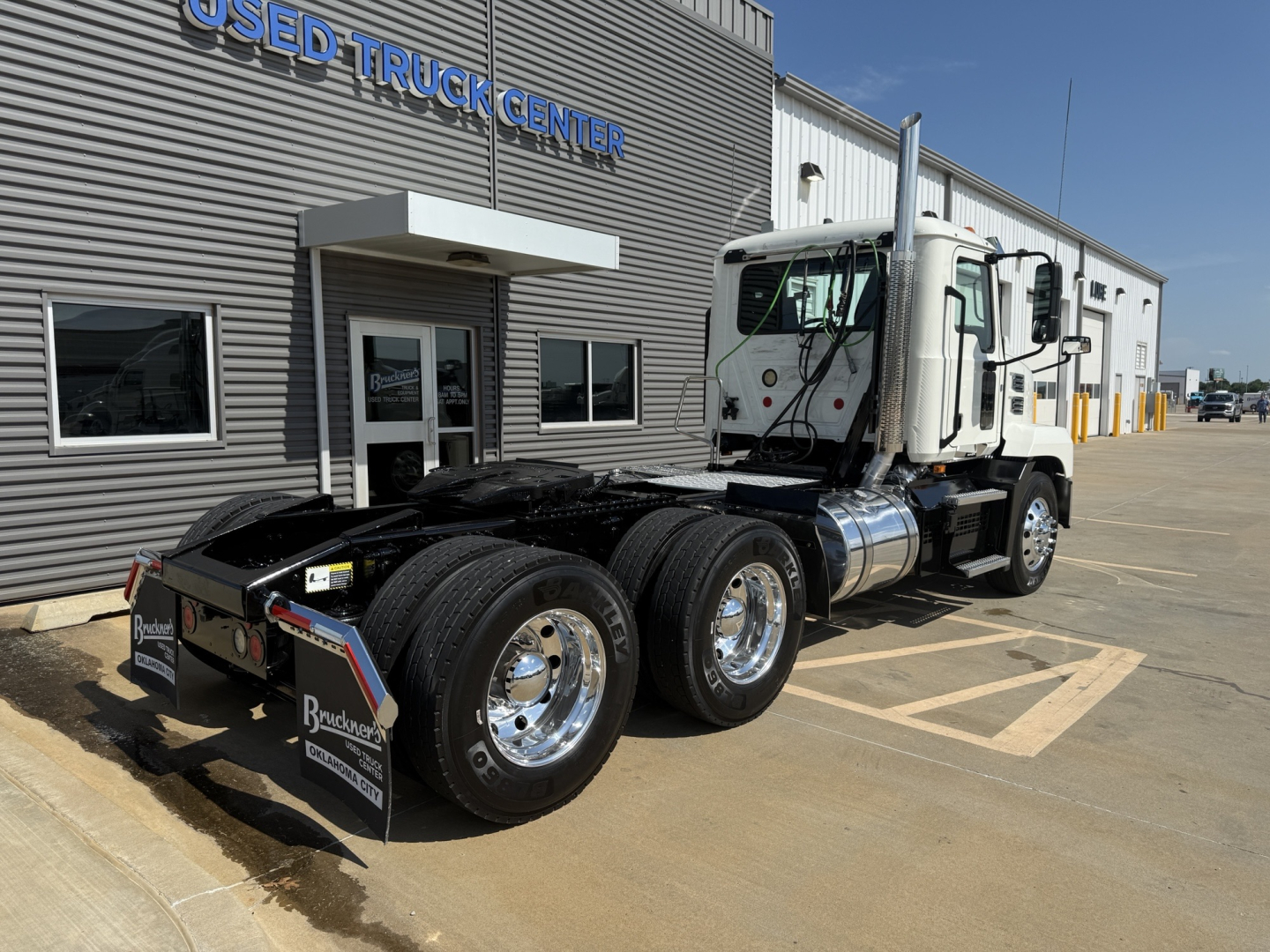Mack AN64T conventional daycab truck at used truck center showing front and rear axles with dual rear tires and chrome wheels.