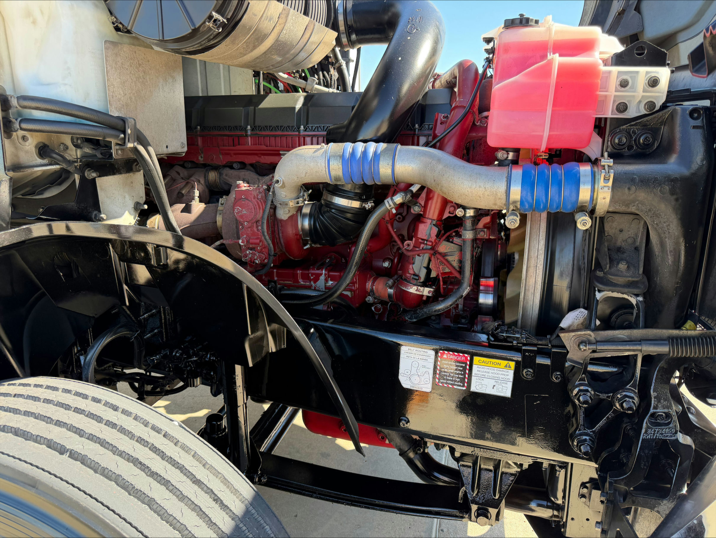 Mack AN64T engine bay showing red engine block, blue silicone hoses, pink coolant reservoir, and black frame.