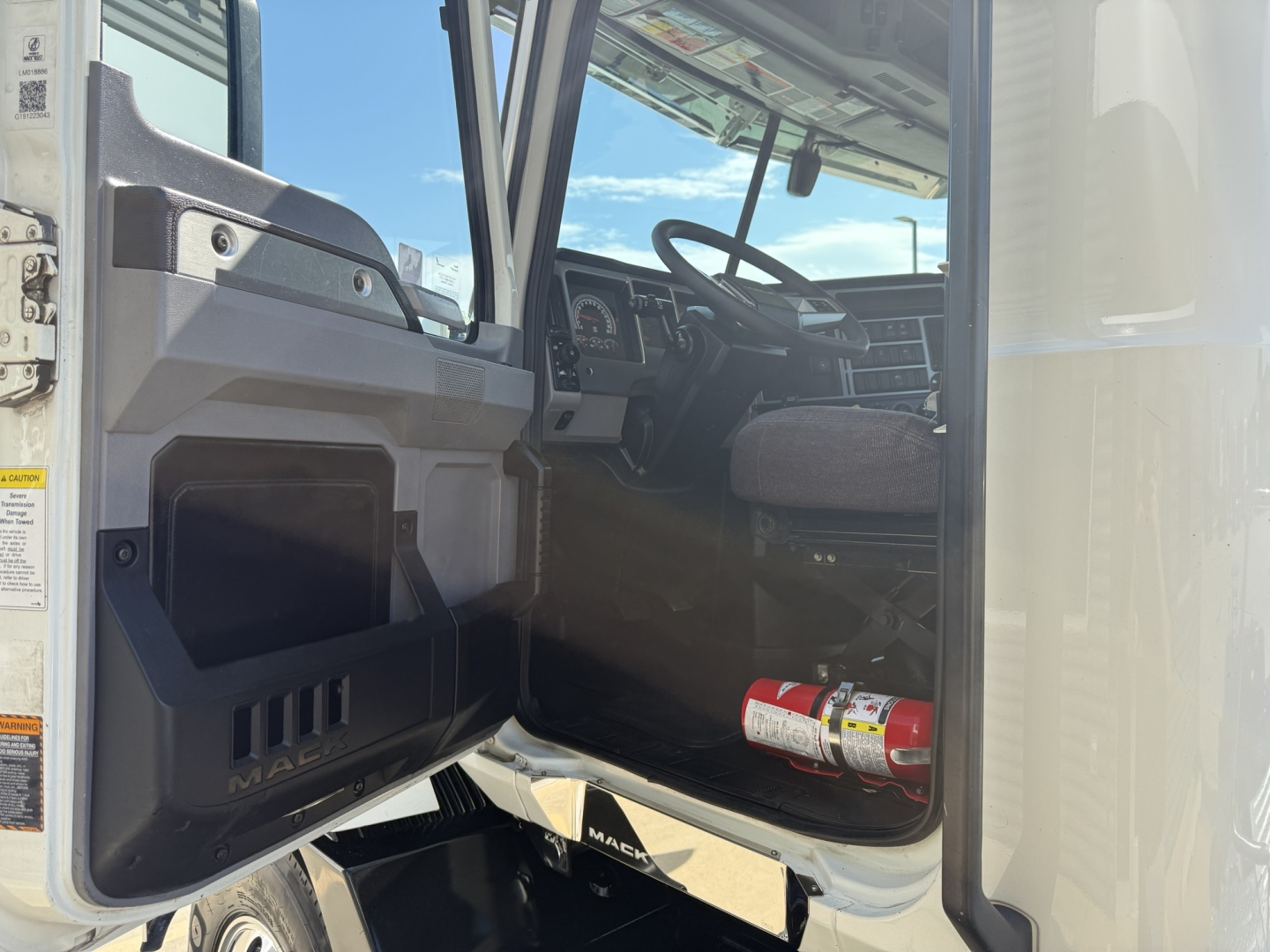 Mack AN64T truck cab interior visible through open door; steering wheel, dashboard, driver seat, and fire extinguisher mounted near door; steps and door frame visible.