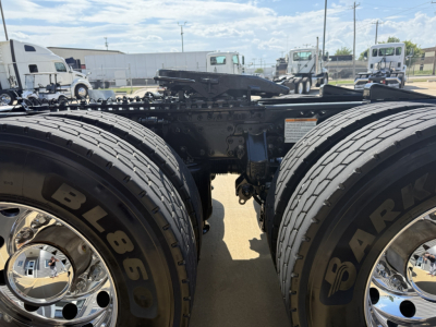 Dual rear wheels of a Mack AN64T with large black tires and chrome rims; chassis frame visible between axles; parking lot with other trucks in background.