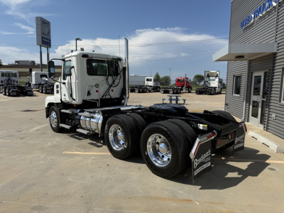 Truck chassis and cab of a 2020 Mack AN64T daycab tractor viewed from the side, showing dual rear axles, fuel tanks, chrome wheels, and a fifth-wheel area; dealership lot in background.