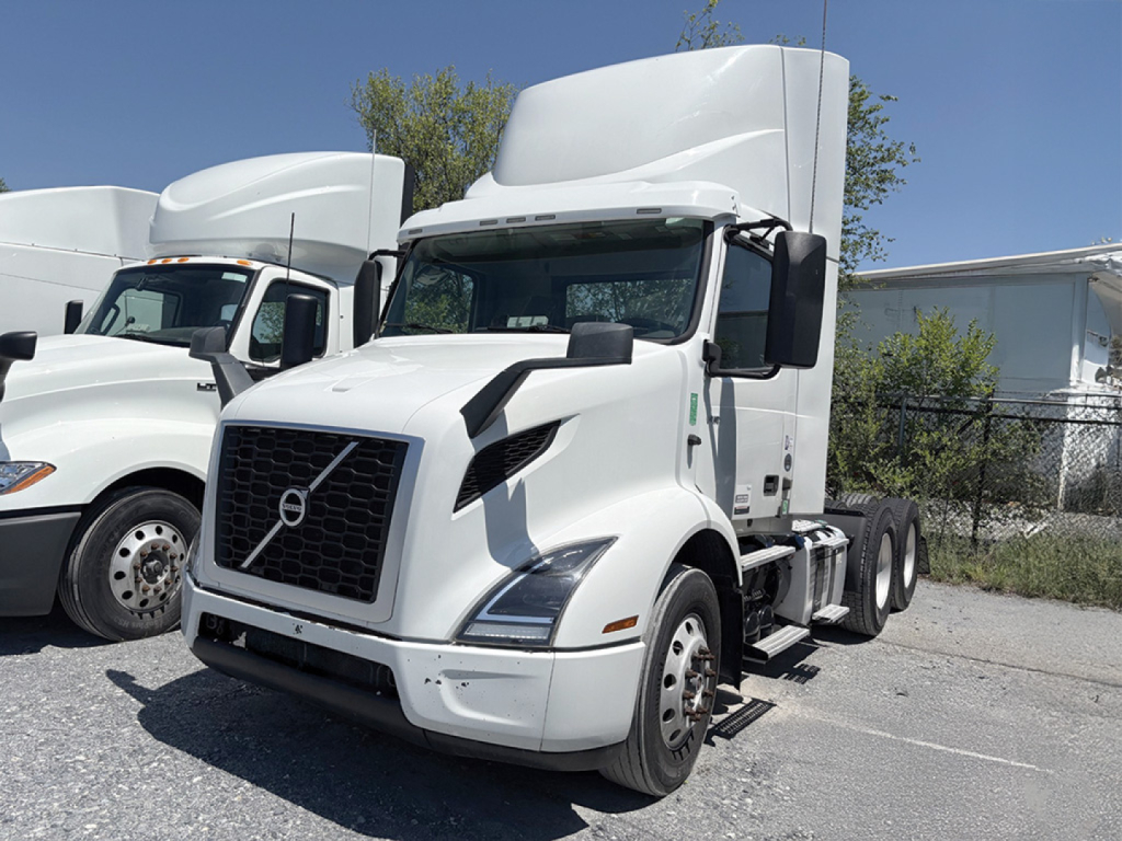 Volvo VNR 300 sleeper cab tractor in a parking lot, front view with black grille, white exterior, two rear axles visible.