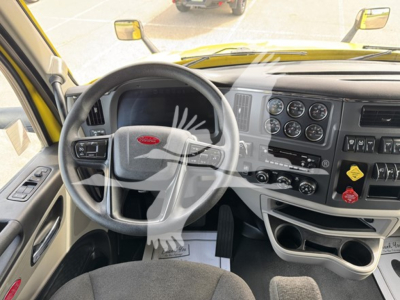 Peterbilt truck interior cockpit showing steering wheel, dashboard with multiple gauges, yellow exterior, gear shifter area and cup holders.