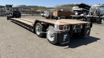 Fontaine Renegade XN20 lowboy trailer showing wooden deck, dual rear axles with black mud flaps, rear lights, and towing hitch area.
