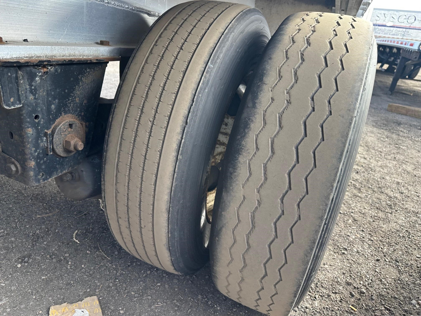 Flatbed trailer axle with two tires and suspension components visible.