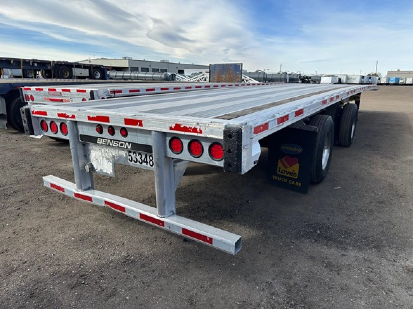 Flatbed trailer showing rear and side with aluminum deck and red/white reflective markings.