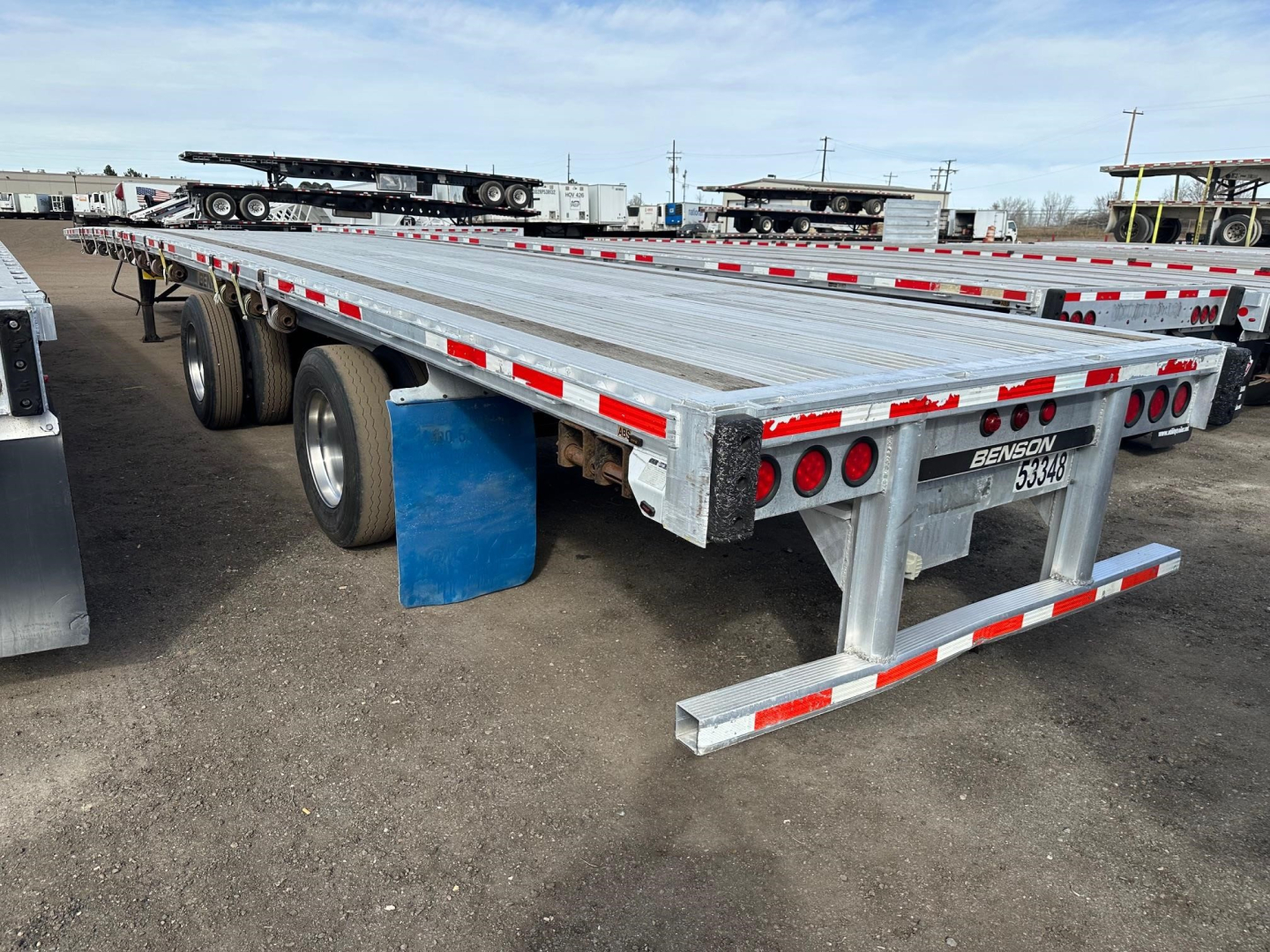 55 ft aluminum flatbed trailer with spread air ride, dual rear axles, metal decking, red/white reflective tape, rear bumper and taillights visible.