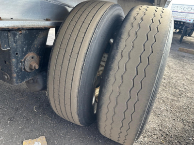 Flatbed trailer axle with two tires and suspension components visible.
