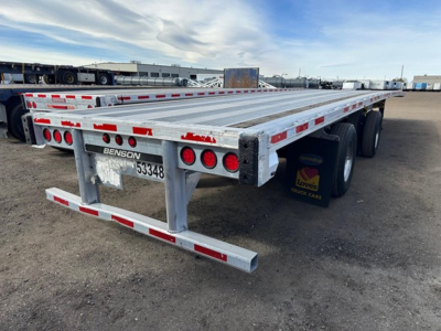 Flatbed trailer showing all-aluminum deck with dual rear axles and Benson tag; red and white reflective tape along edges, multiple taillights, VIN area visible.