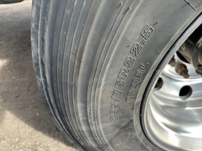 Flatbed trailer wheel and tire with tire markings visible: 295/75R22.5 (R22.5) and 8-225-? Not fully clear; shows metal wheel and hub.