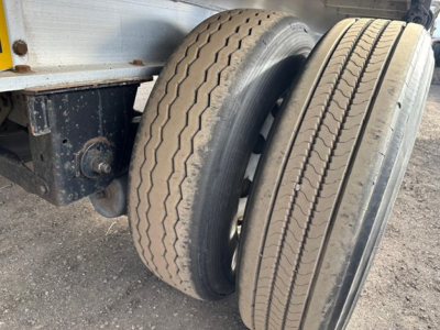 All-aluminum flatbed trailer wheel area showing tandem tires and suspension mount with worn tread patterns.