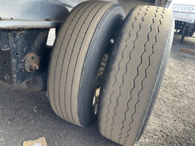 Trailer axle with two tires on a 53' aluminum flatbed showing wheel rims and suspension components.