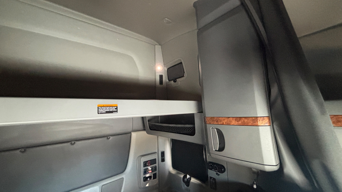 Interior view of a 2021 International LT625 truck sleeper compartment showing upper storage shelf, side panel, and control panel.