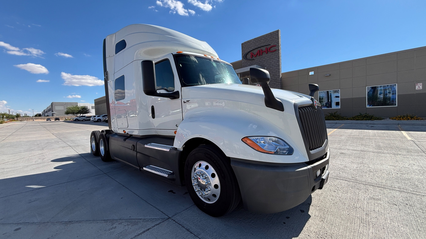 Truck cab and front of a white 2021 International LT625 semi-truck with black bumper, chrome wheels, and aerodynamic sleeper. Distinct International grille, side mirrors, and windows visible.