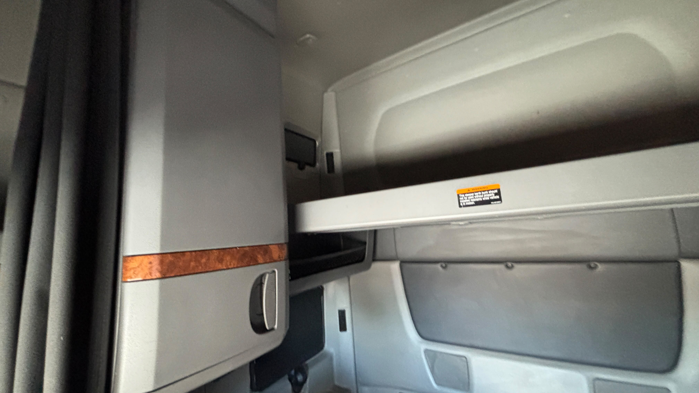 Interior view of a truck cab showing a storage compartment and shelves with a small warning label, part of an International LT625 sleeper cab.