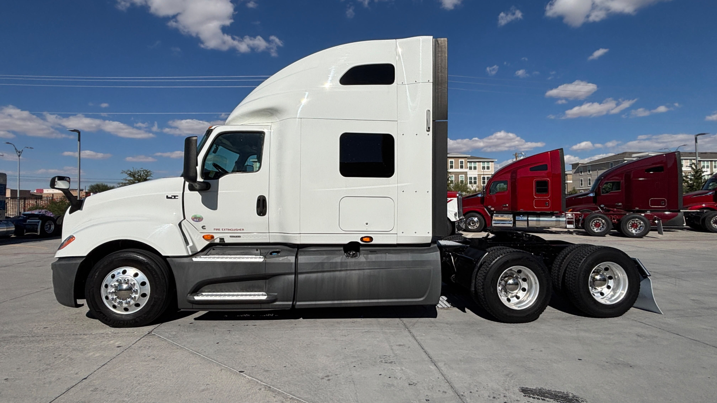 Truck tractor in a side profile showing a white International LT625 sleeper cab with three rear axles and chrome fuel tanks.