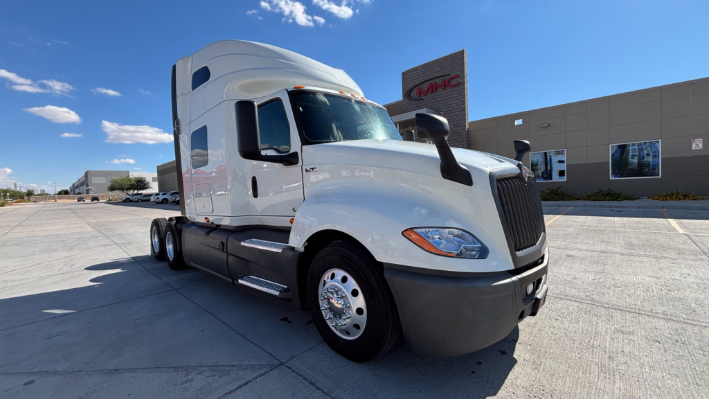 Truck cab and front of a white 2021 International LT625 semi-truck with black bumper, chrome wheels, and aerodynamic sleeper. Distinct International grille, side mirrors, and windows visible.