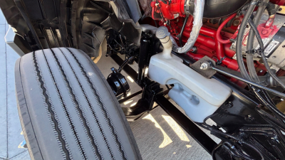 Truck engine bay showing coolant reservoir and engine components in a 2021 International LT625. Visible: white coolant reservoir, red engine block, black chassis, hoses, and metal brackets.
