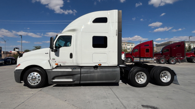 Truck tractor in a side profile showing a white International LT625 sleeper cab with three rear axles and chrome fuel tanks.
