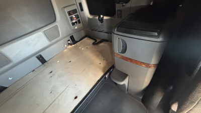 Truck cab interior showing sleeper area with wooden floor panel and control panels on left side.