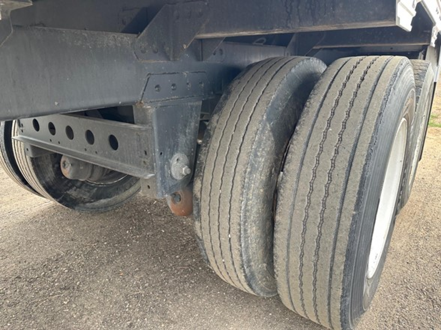 Trailer wheel end showing dual rear axles on a Timpte hopper trailer with black frame and tires, portion of the underside and suspension visible.