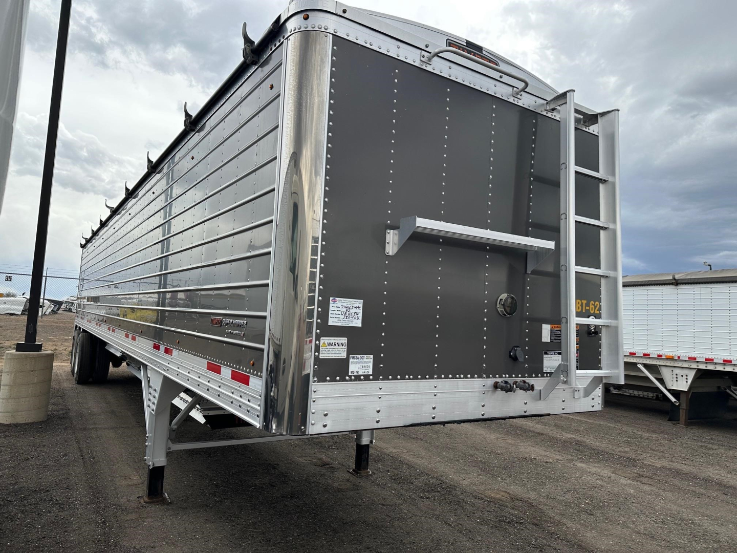 Trailer side and rear of a 2024 Timpte Super Hopper W 78 inch sides showing riveted metal siding, rear ladder, high-visibility safety decals, landing gear, and rear hopper door.