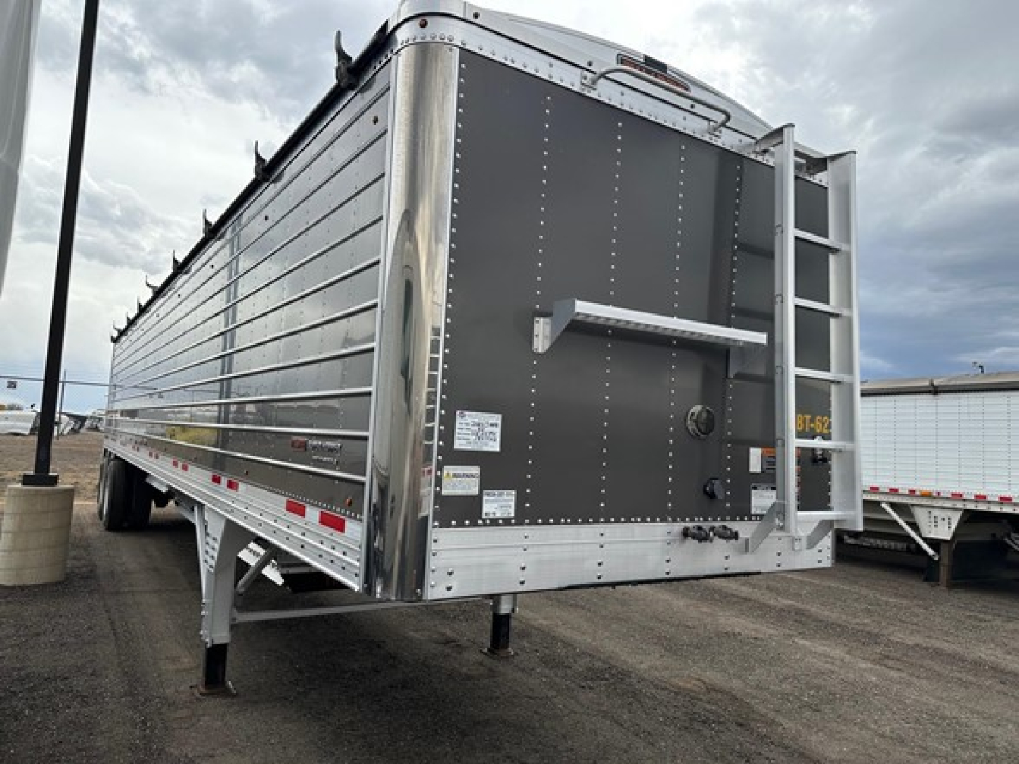 Trailer rear with vertical riveted metal sides of a 2024 Timpte Super Hopper, rear hatch and ladder visible, stock/ID plates and warning decals on tailgate.
