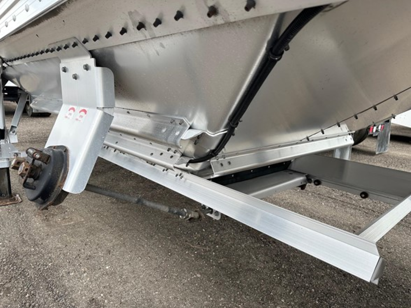 Timpte Super Hopper trailer undercarriage showing axle support and hitch area with structural aluminum beams and hydraulic line.