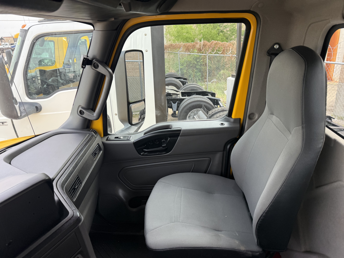 Interior view of a 2019 International LT truck cab showing grey fabric seat, front passenger area, window controls, and yellow exterior frame.