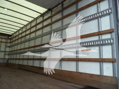 Truck trailer interior with metal side walls and wooden runners; faint sticker label on wall