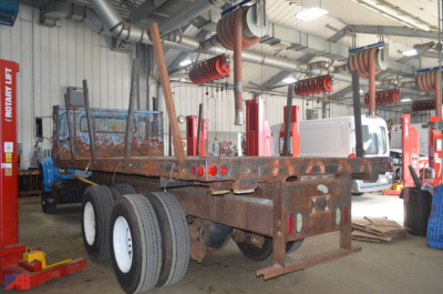 1992 International 4900 flatbed truck chassis inside a workshop with red equipment and hanging hoses.