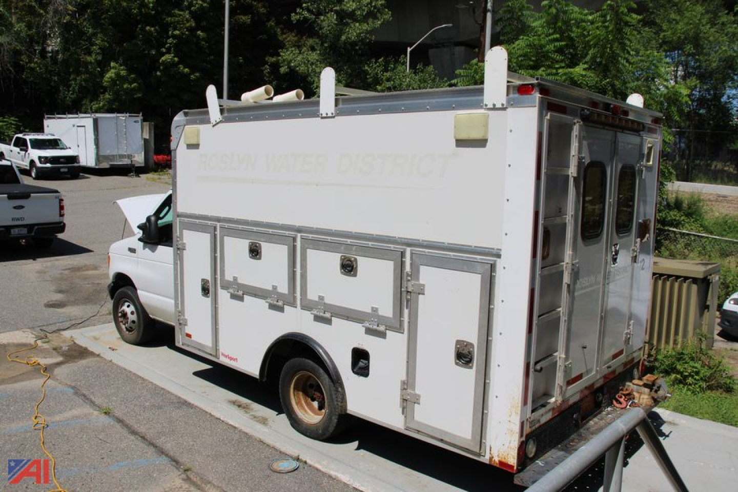 Box truck rear view showing storage compartments and side windows, with faded text on rear doors and a detached bumper hose on ground.
