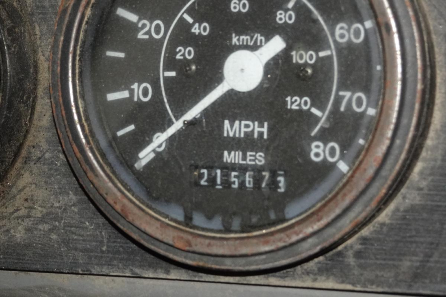 Gauge cluster showing speedometer with MPH and km/h markings; odometer reads 215673 miles; circular bezel with metal rim.