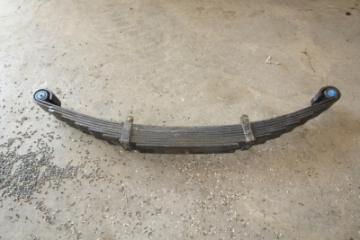 Leaf spring axle component with blue bushings and metal straps, viewed on concrete floor.