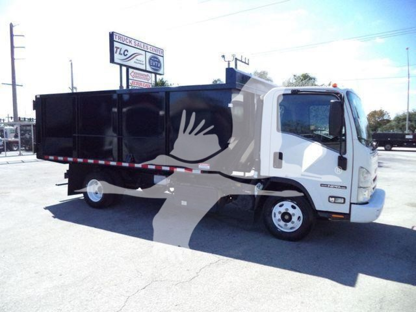 Isuzu NPR HD dump truck in white cab and black dump bed, side view, with stock yard background.