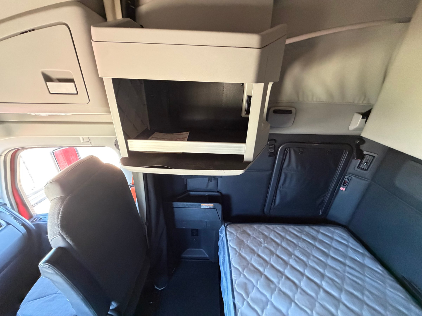 Kenworth T680 sleeper cab interior showing upper storage cabinet and bunk area with quilted mattress pad.