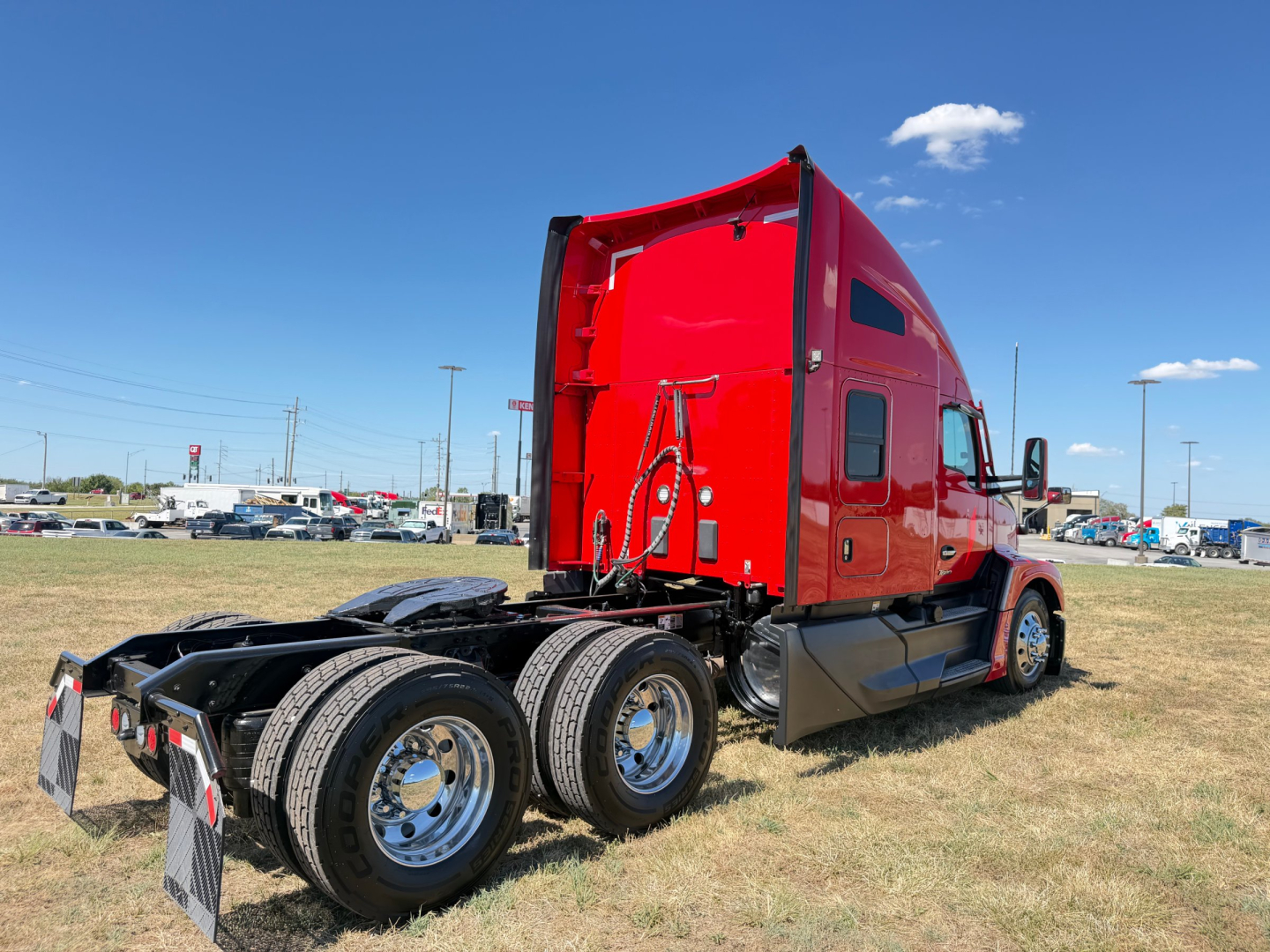 Kenworth T680 tractor rear-left side view showing red cab and dual rear axles with chrome wheels.