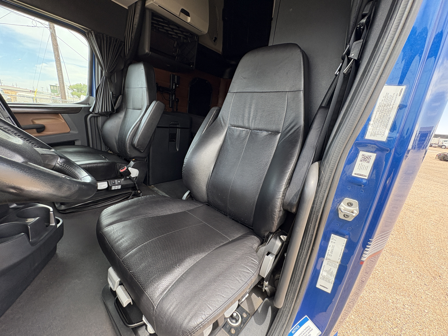 Cab interior of a Freightliner Cascadia 126 showing driver seat and passenger seat in view, with door frame and fabric upholstery visible